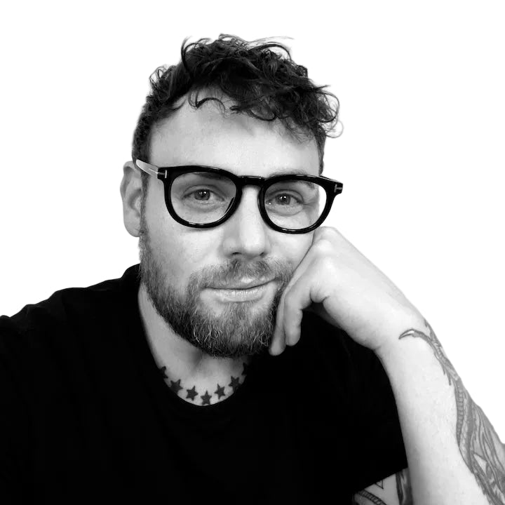 Black and white portrait of a man with glasses and tattoos on a plain background